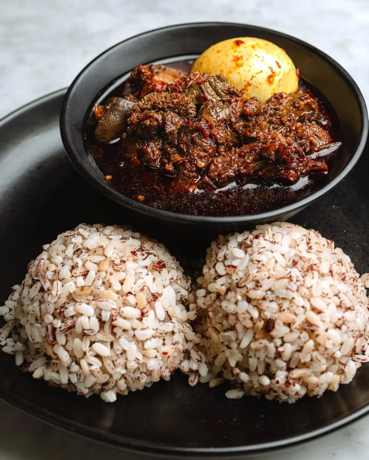 Ofada rice served with ayamase stew and an egg