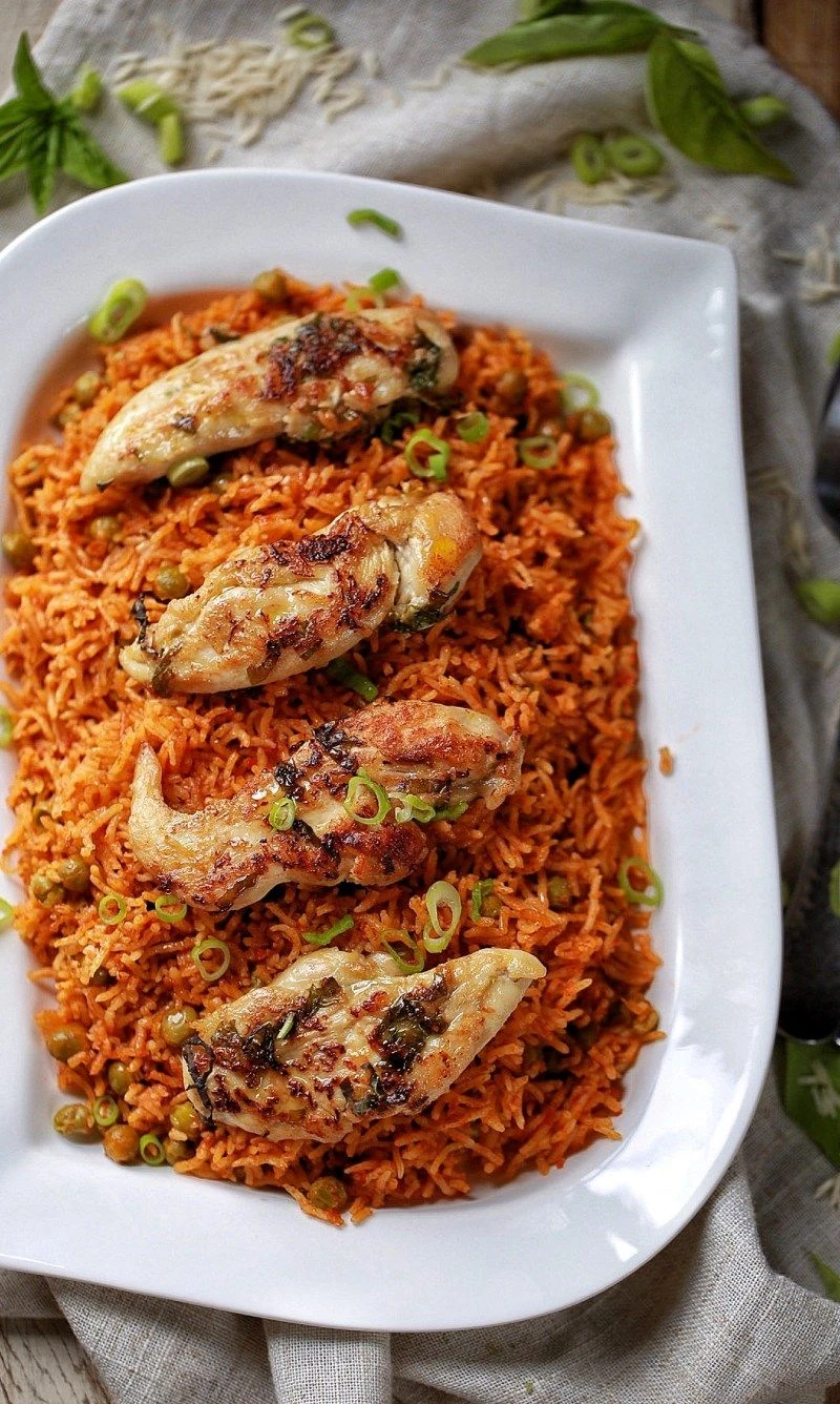 Jollof rice topped with grilled chicken wings on a white serving plate